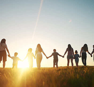 A silhouette of a large group of people holding hands walking during sunset in the park.